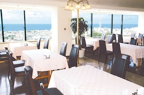 A restaurant with multiple tables and chairs, large windows with a city view, and a central light fixture. - Hotel Tamai (Aki)