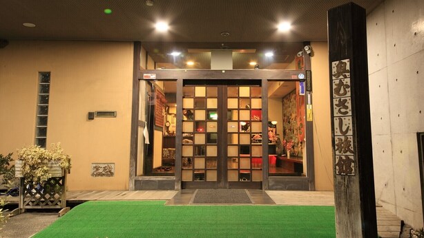 A hotel entrance with a traditional Japanese gate, a small outdoor area with artificial grass, and a wooden post with Japanese characters. - Okumusashi Ryokan (Hanno)