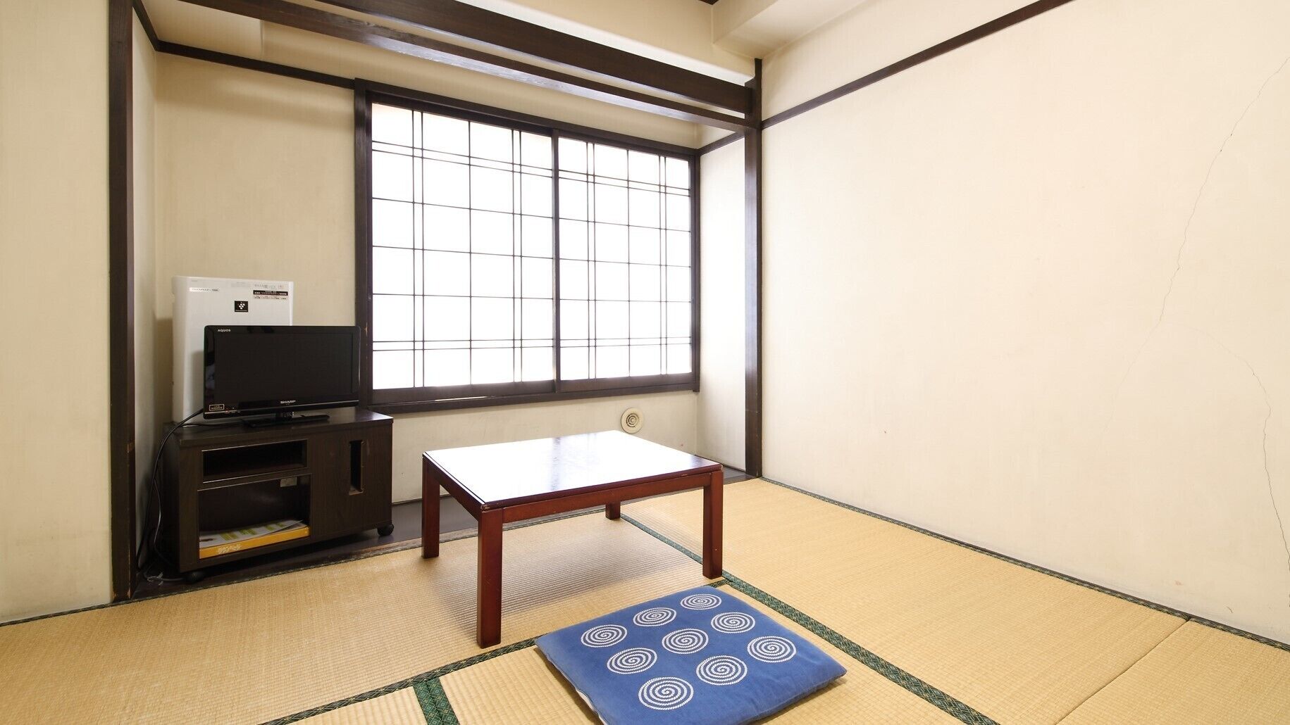 Quarto com piso de tatame, uma mesa de madeira baixa, televisão sobre suporte e uma janela grande com grades.
