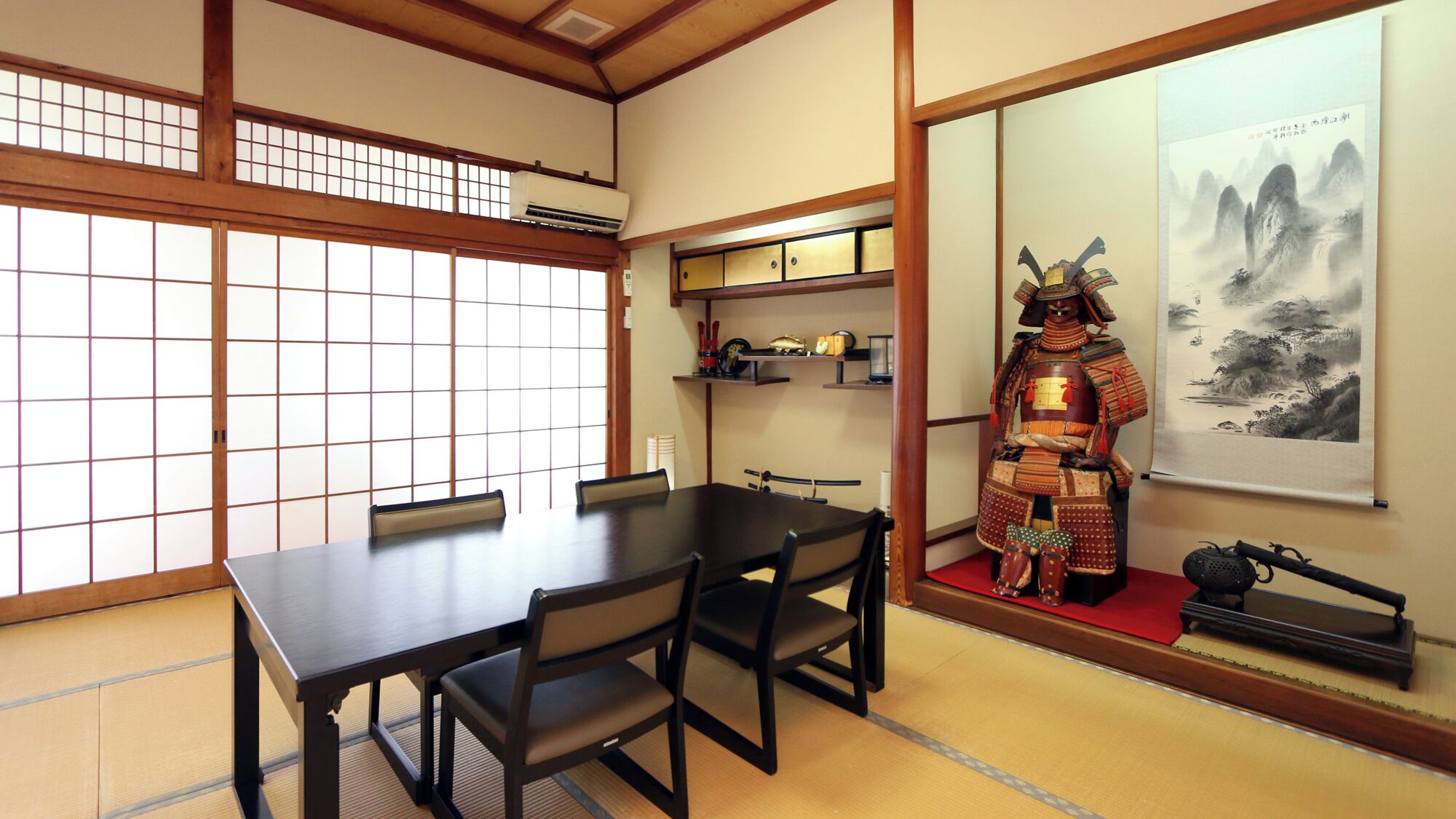 A traditional Japanese room with tatami flooring, a low table with chairs, a shoji screen, and a mounted samurai armor display.