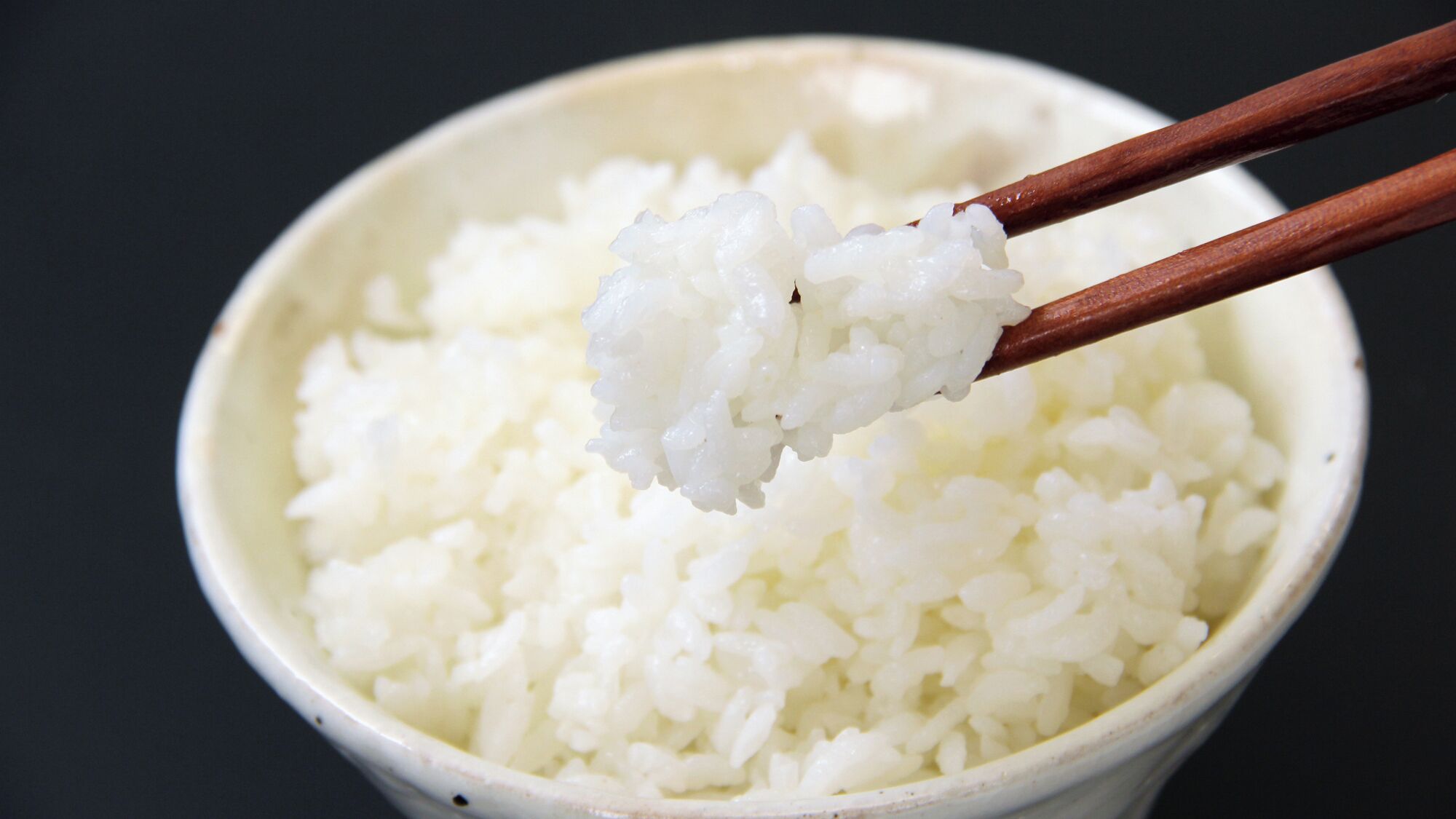 A bowl of white rice with chopsticks lifting a portion.