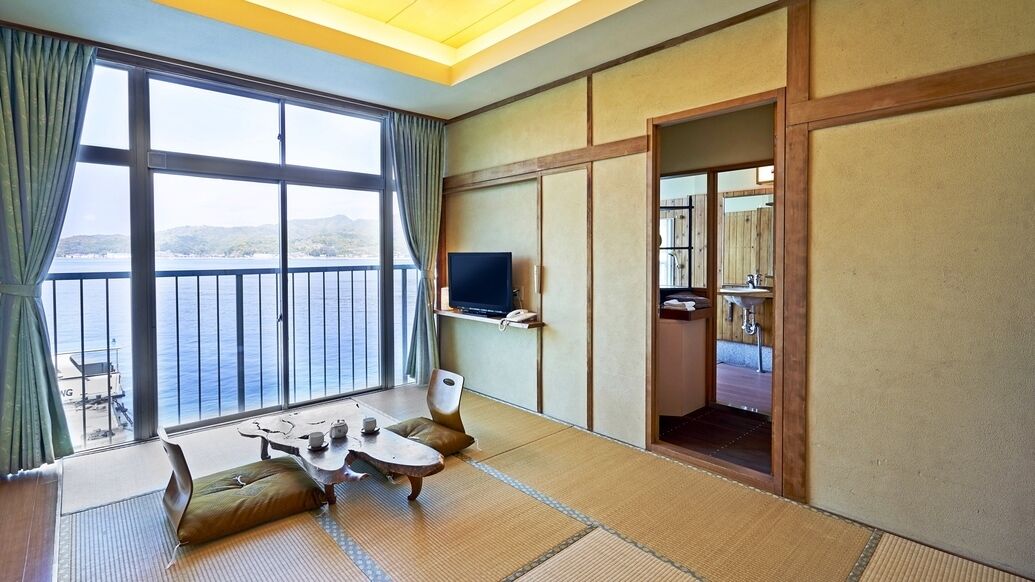 Ein Zimmer mit großem Fenster, Fernseher, kleinem Tisch und Meerblick.