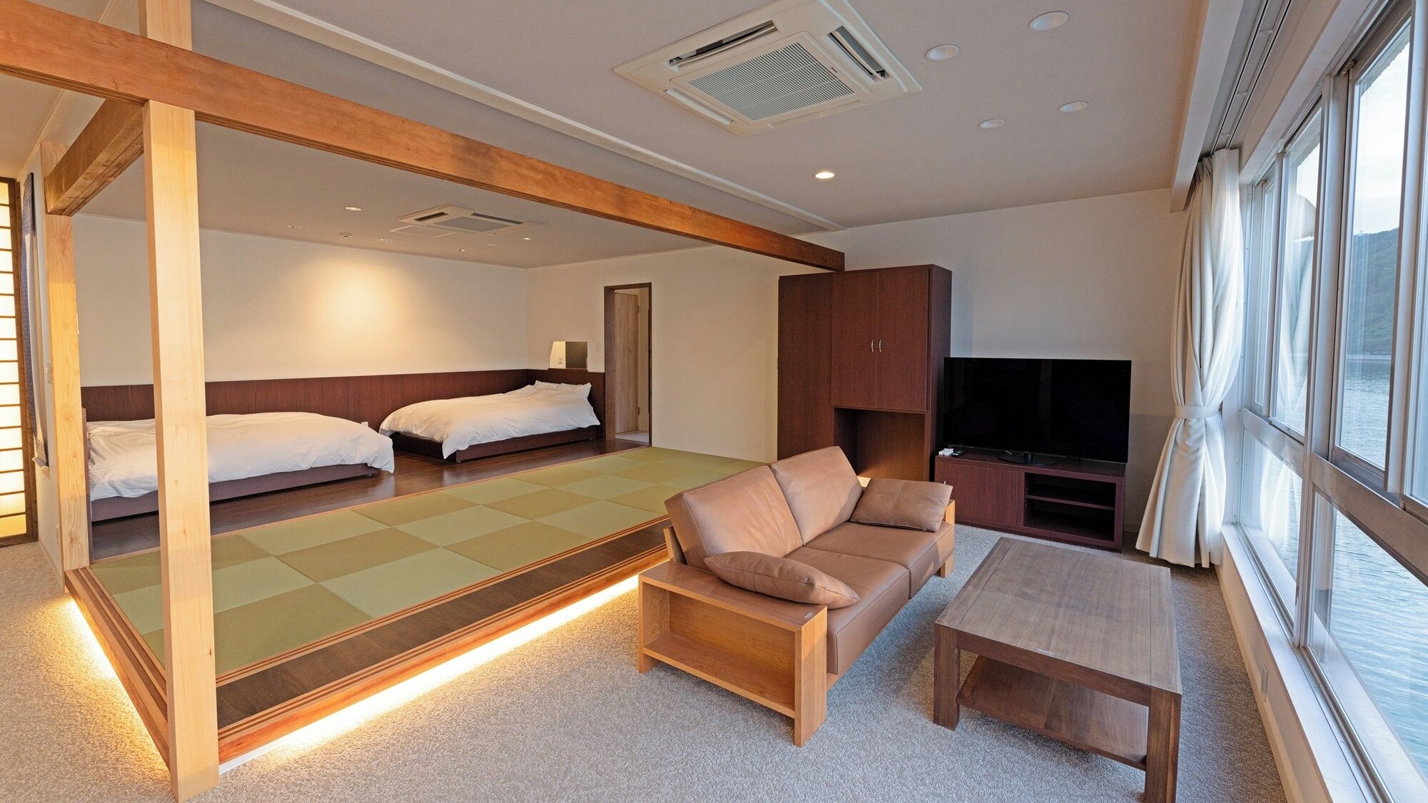 Una habitación de hotel moderna con sofá, una mesita, un televisor y una cama con cabecero de madera.