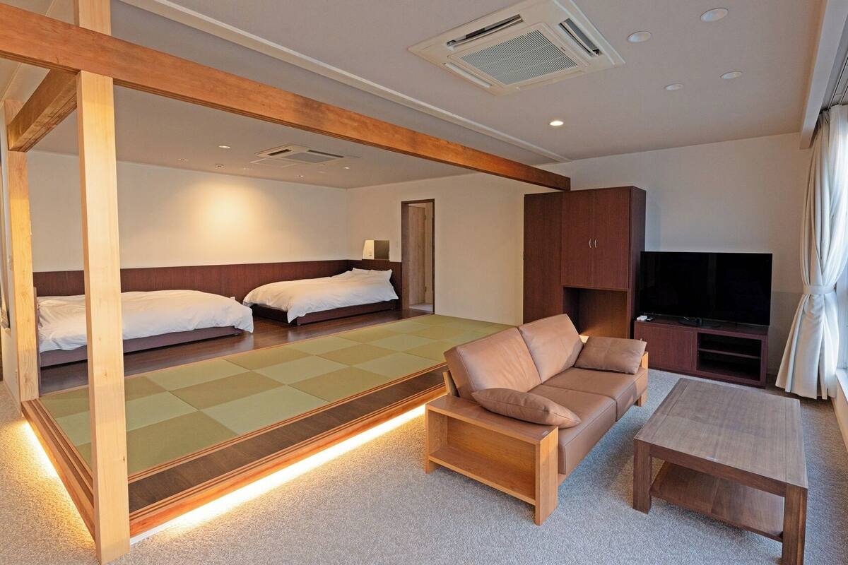 Ein modernes Hotelzimmer mit einer Couch, einem kleinen Tisch, einem Fernseher und einem Bett mit einem Holz-Kopfteil.