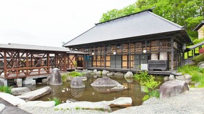 A traditional Japanese building with a tiled roof, wooden beams, and a stone pond with rocks.