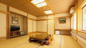 Una habitación tradicional japonesa con suelo de tatami, una mesa de madera para comer, un televisor y puertas correderas.