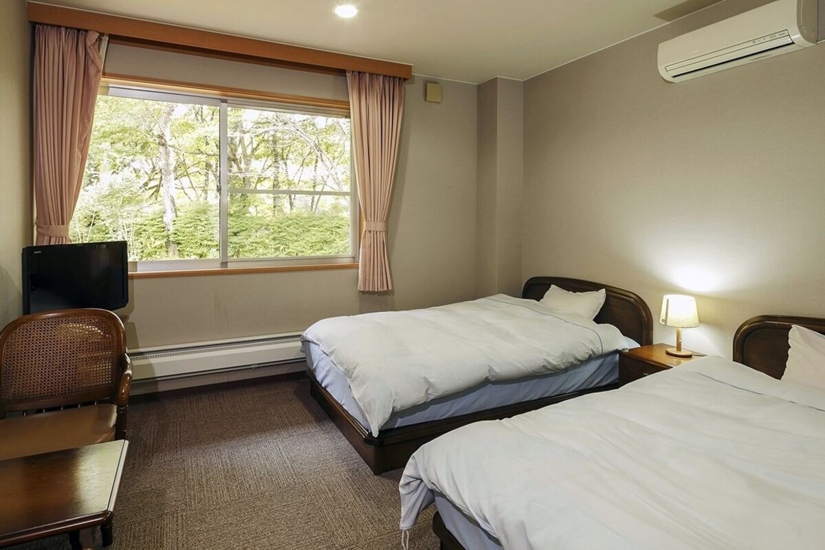 A hotel room with two beds, a television, a chair, and a window with curtains.