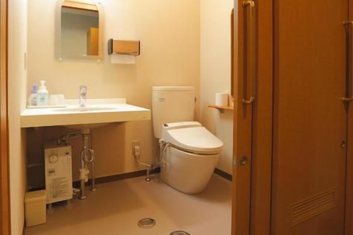 A small bathroom with a toilet, sink, and mirror. There is a pair of slippers on the floor.