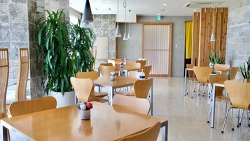 Un comedor moderno con mesas y sillas de madera, plantas en macetas y una planta verde grande en el centro.