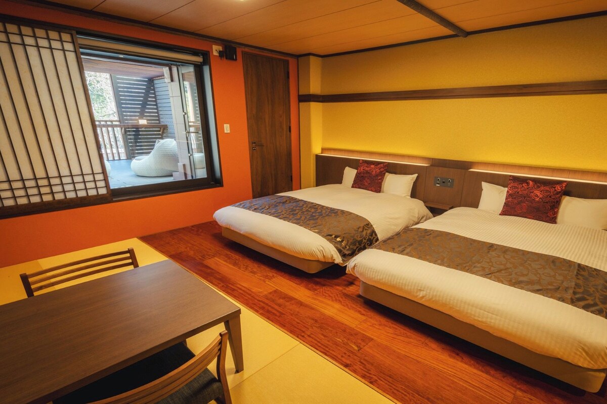 A hotel room with two beds, a wooden table, and a sliding shoji screen.
