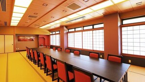 Un salón de conferencias con una larga mesa, sillas rojas y ventanas amplias.