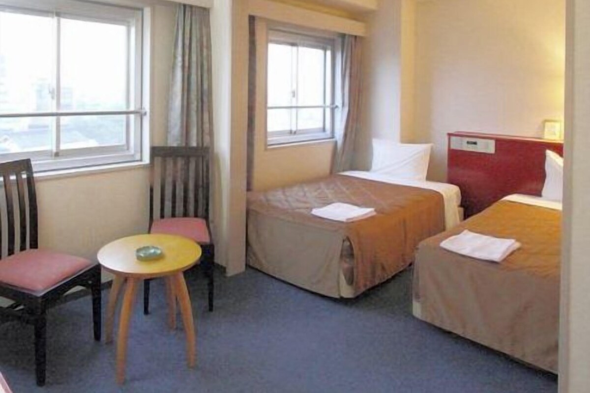 A hotel room with two beds, a small table, and a chair.