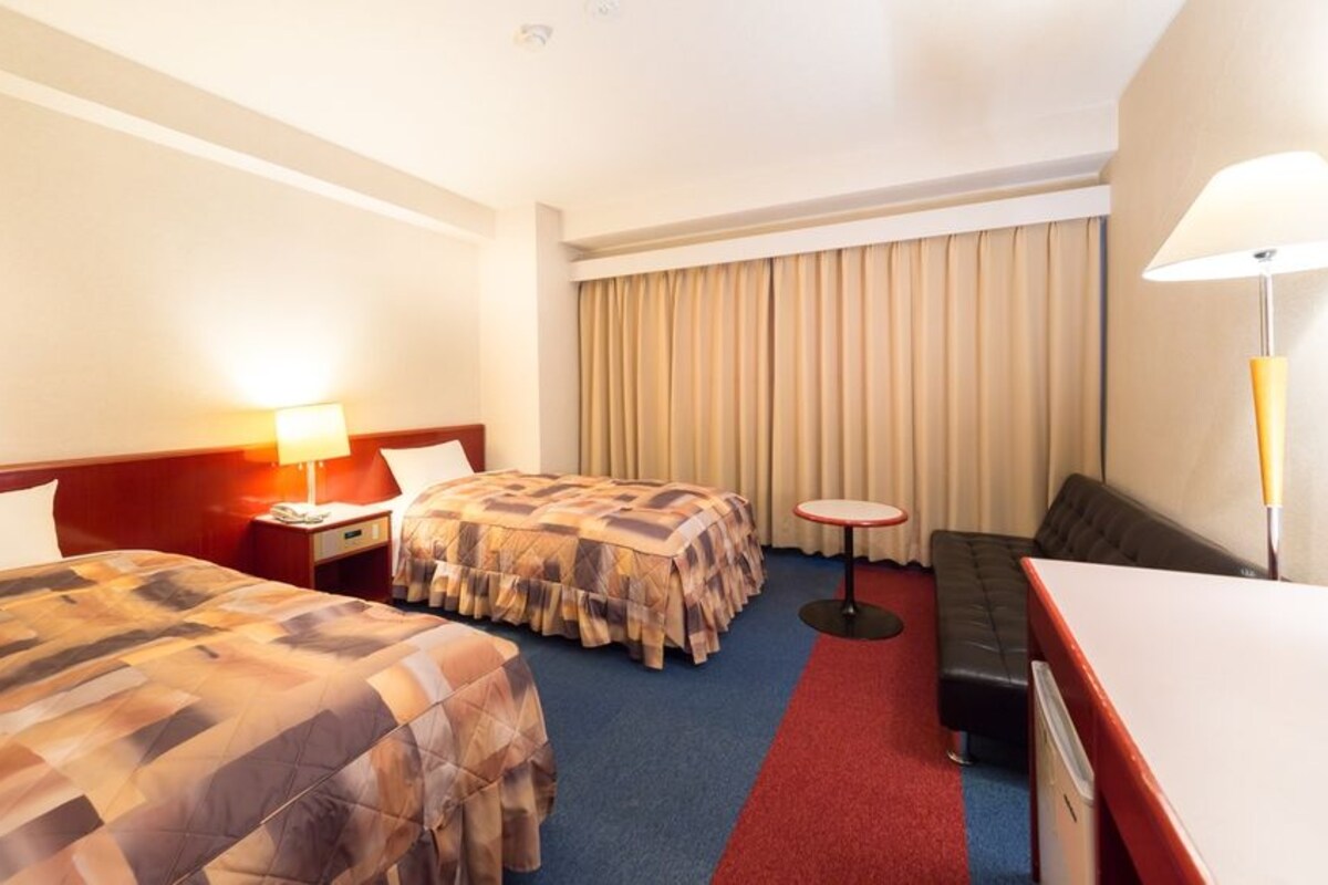 A hotel room with two beds, a desk, a chair, a small round table, and a sofa.