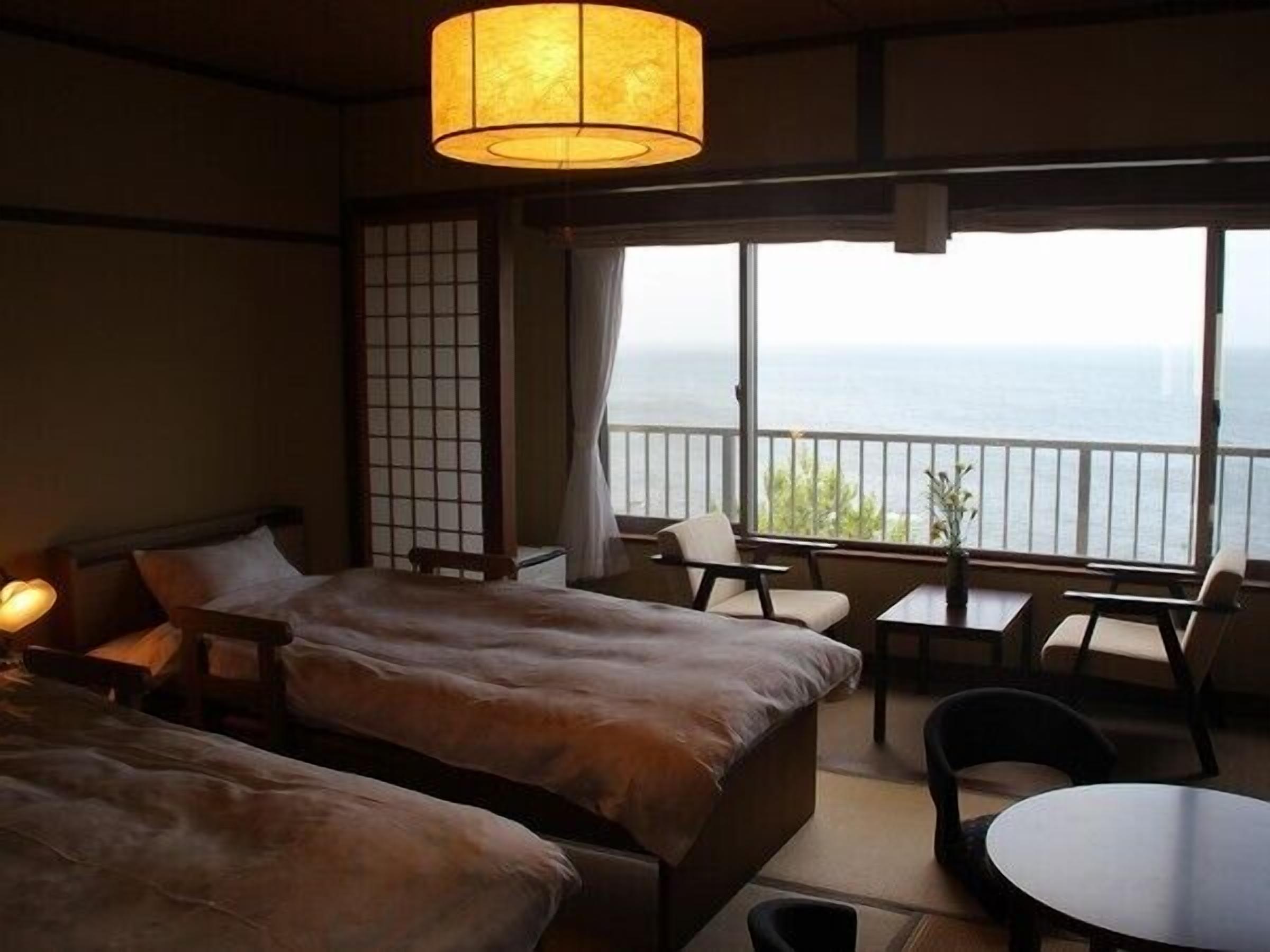 Habitación de hotel con cama, una mesita, una silla y vista al mar.