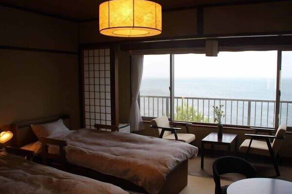 A hotel room with a bed, a small table, a chair, and a view of the sea.