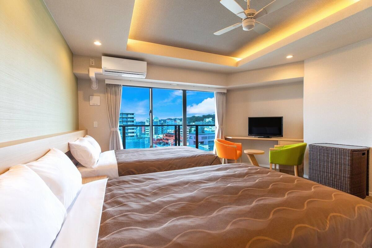Une chambre d’hôtel avec deux lits, une télévision, une petite table et une vue sur la ville.