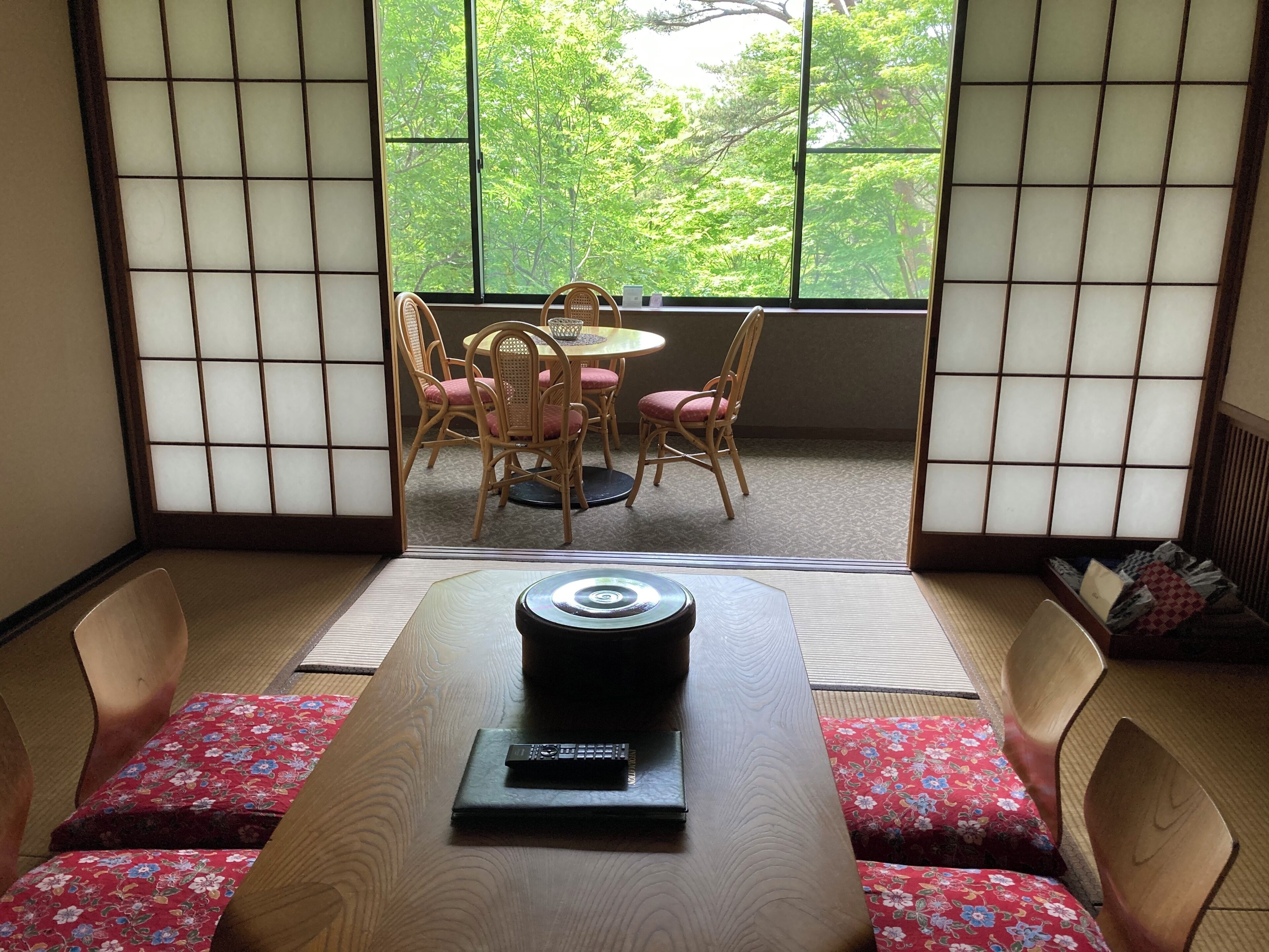 A traditional Japanese room with tatami flooring, a low table with a remote control, and a view of a garden through a shoji screen.
