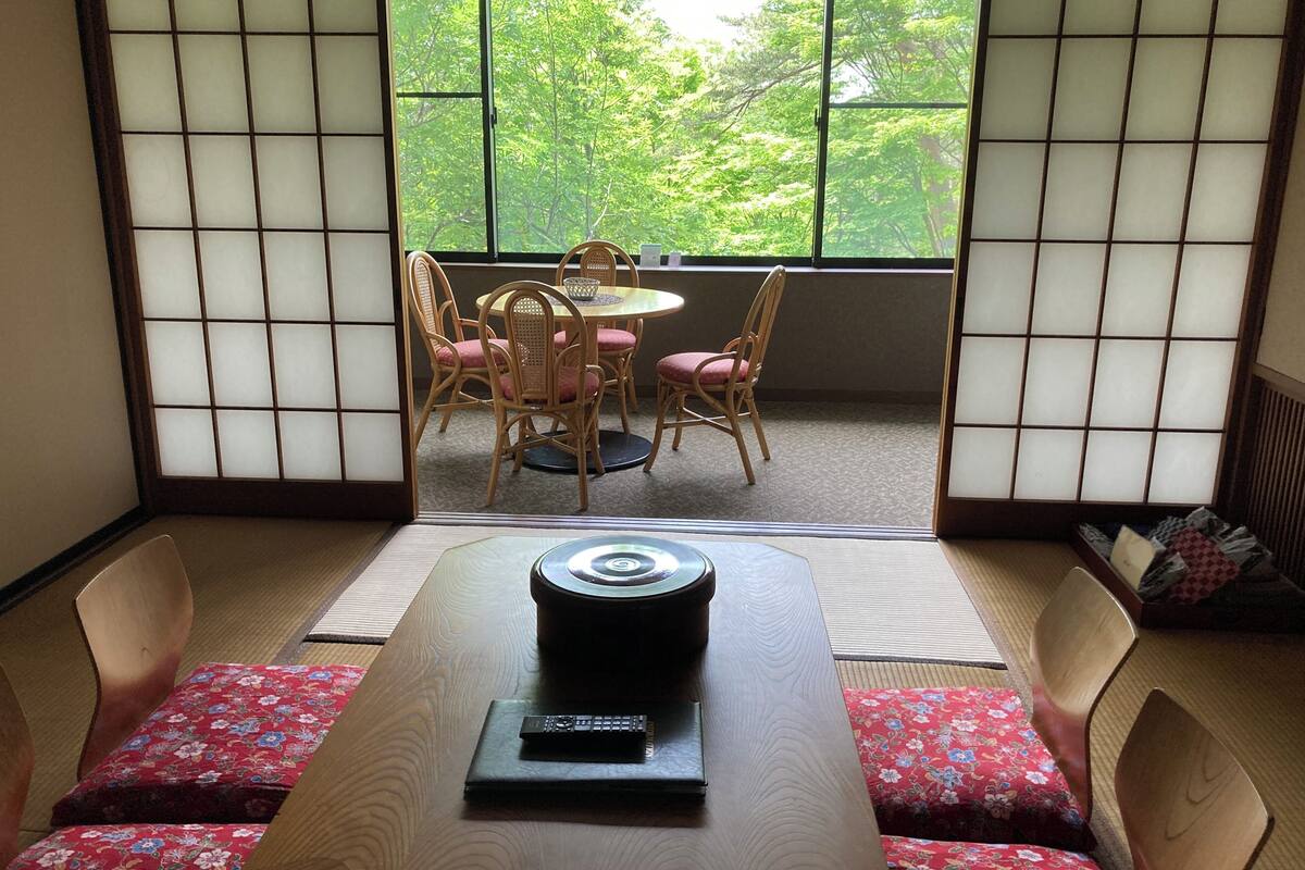 Una habitación japonesa tradicional con suelo de tatami, una mesa baja con un control remoto y vistas a un jardín a través de un celosía shoji.