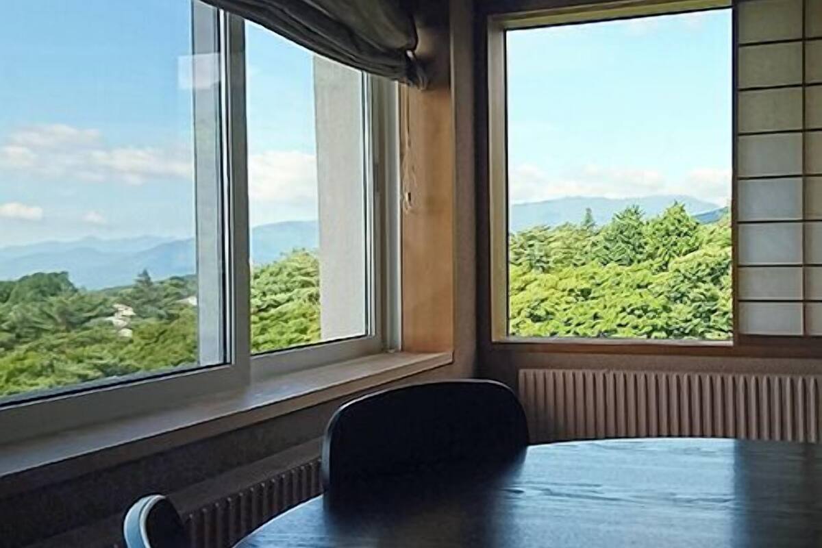 Una habitación con un gran ventanal, una mesa y una silla.