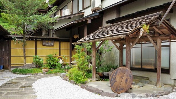 A traditional Japanese building with a wooden structure, a stone pathway, and various plants. - Ryokan Tsurutomiyashiki (Shiiba-son)