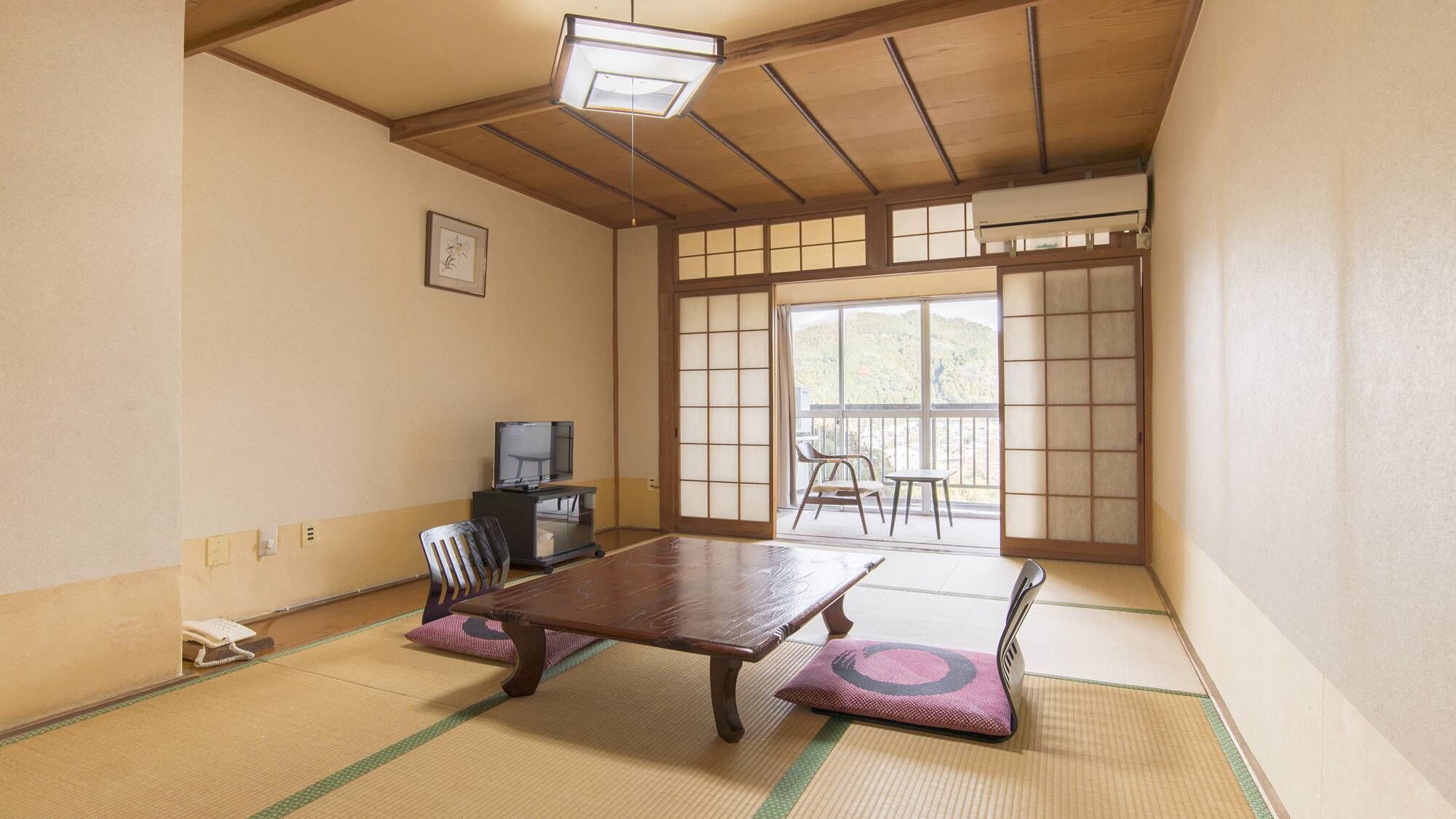 Une pièce de style japonais traditionnel, avec un sol recouvert de tatamis, une table basse, un téléviseur et une porte coulissante donnant sur un balcon.