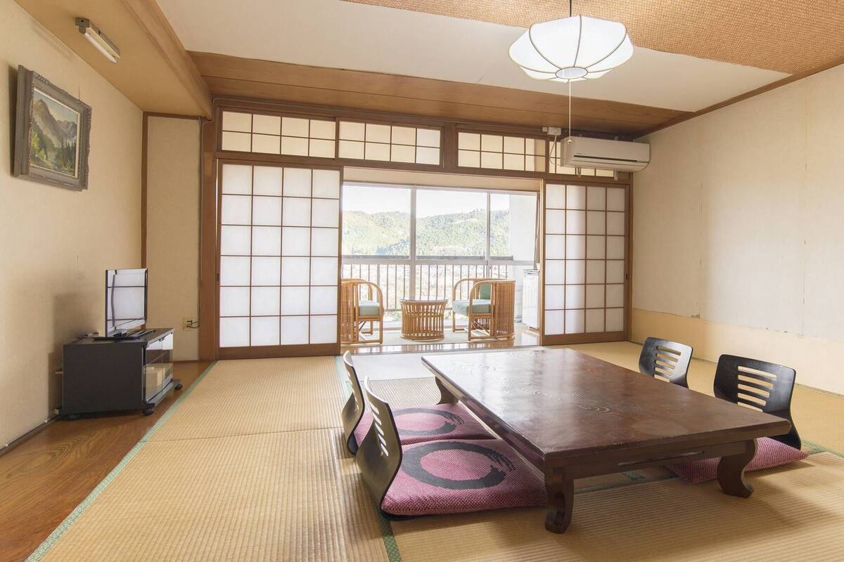Ein traditioneller japanischer Raum mit Tatami-Bodenbelag, einem niedrigen Tisch, Stühlen und einer Schiebetür mit Blick.