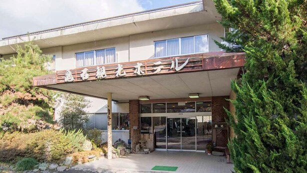 Un edificio con un letrero en idioma extranjero, un acceso cubierto y un pequeño jardín.