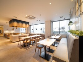 A modern restaurant interior with a central island, multiple seating options including tables and a sofa, and large windows providing natural light.
