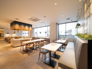 A modern restaurant interior with a central island, multiple seating options including tables and a sofa, and large windows providing natural light. - Super Hotel Anan Shiyakushomae (Anan)
