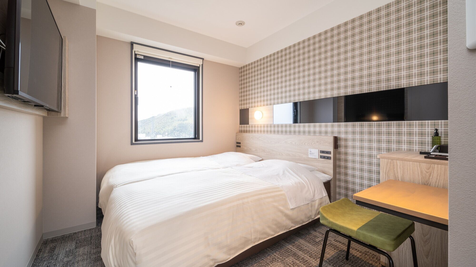 A hotel room with a bed, a small table, a chair, a TV, and a window with a view.