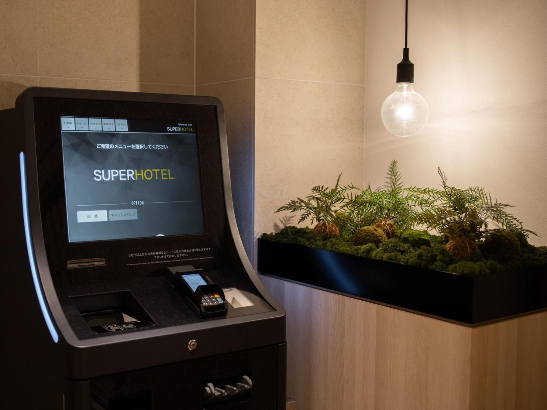 A self-service kiosk with a digital display for hotel check-in, a payment terminal, and a small plant display.