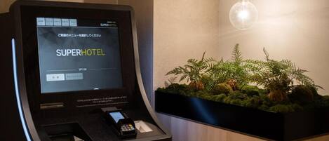 A self-service kiosk with a digital display for hotel check-in, a payment terminal, and a small plant display.
