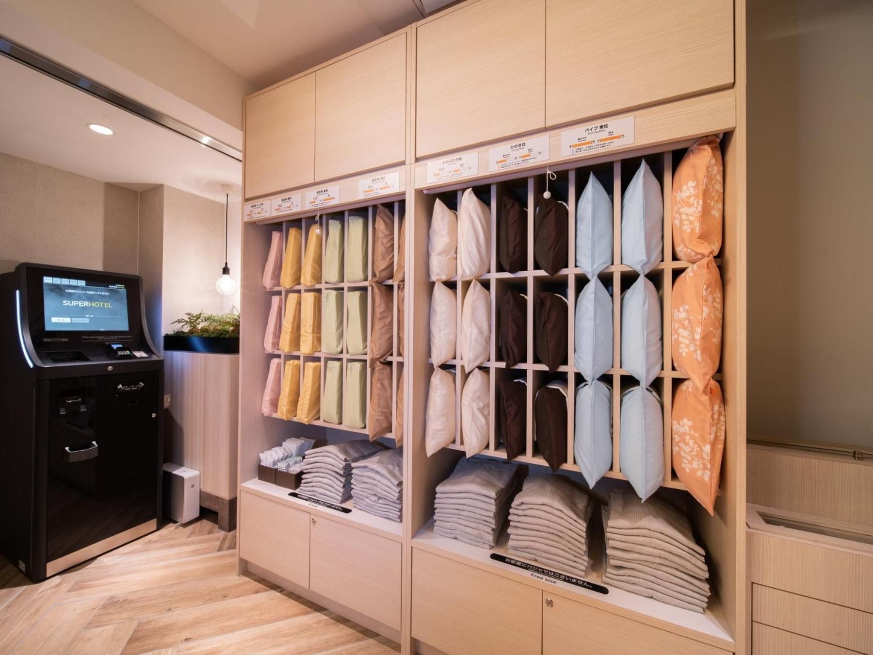 A hotel room with a bed, a TV, and a storage unit with folded towels and pillows.