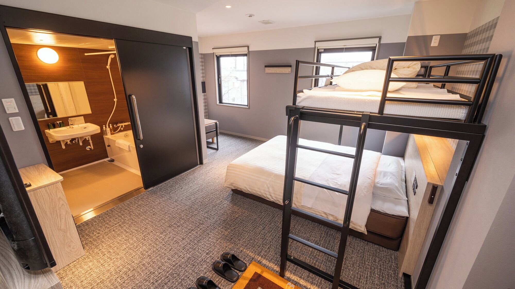 A compact hotel room with bunk beds, a bathroom with a sink, and a shower.