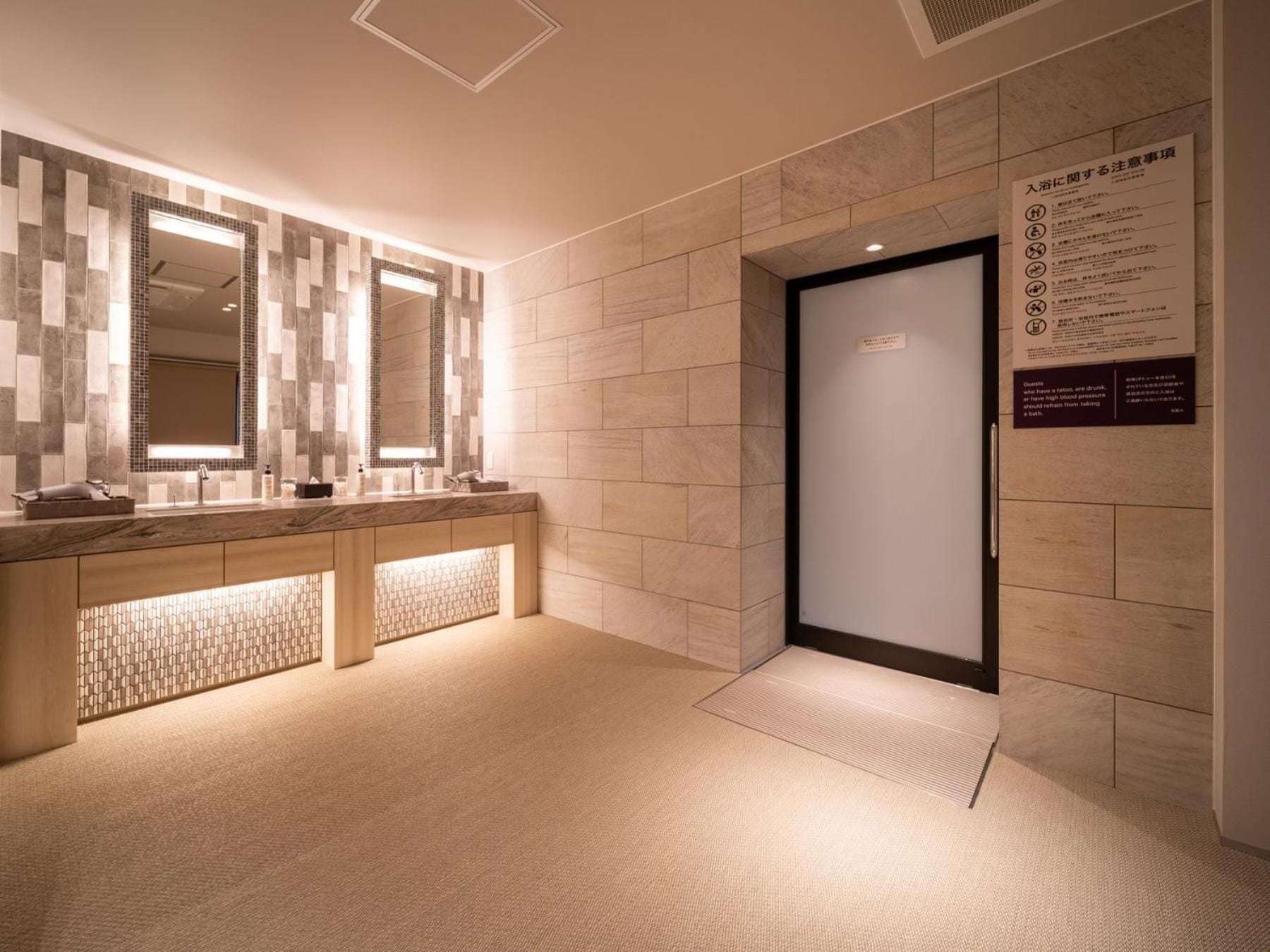 Een moderne badkamer met een grote spiegel, een wastafel en een toilet. Er hangt een bord op de muur met tekst en symbolen.