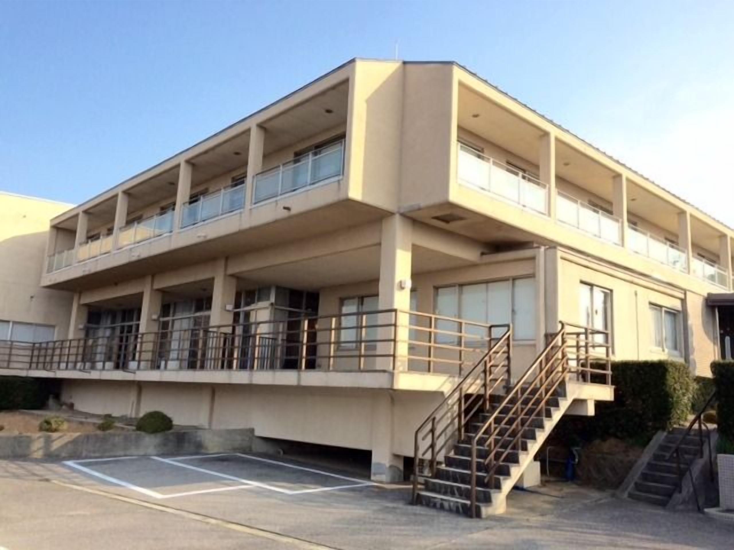 A multi-story building with balconies, a parking area, and a staircase.