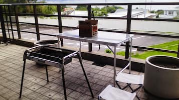 A balcony with a grill, a table, chairs, and a potted plant.
