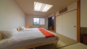 A traditional Japanese-style bedroom with a bed, futon, sliding doors, and a window with a view. - Ryokan Kozyo (Yabu)