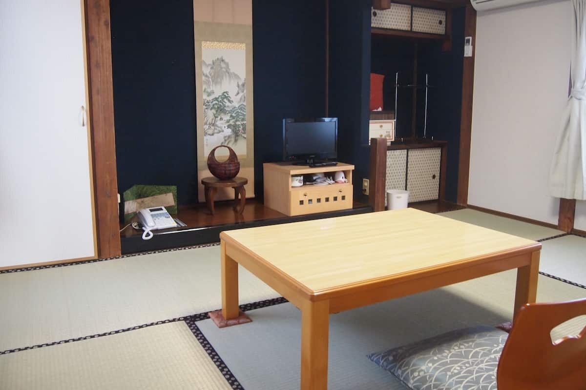 A traditional Japanese room with tatami flooring, a wooden table, a television on a stand, and a sliding door.
