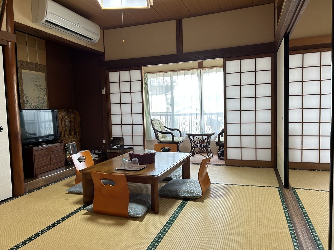 A traditional Japanese room with tatami flooring, a tatami mat table, wooden furniture, a television, and sliding doors.