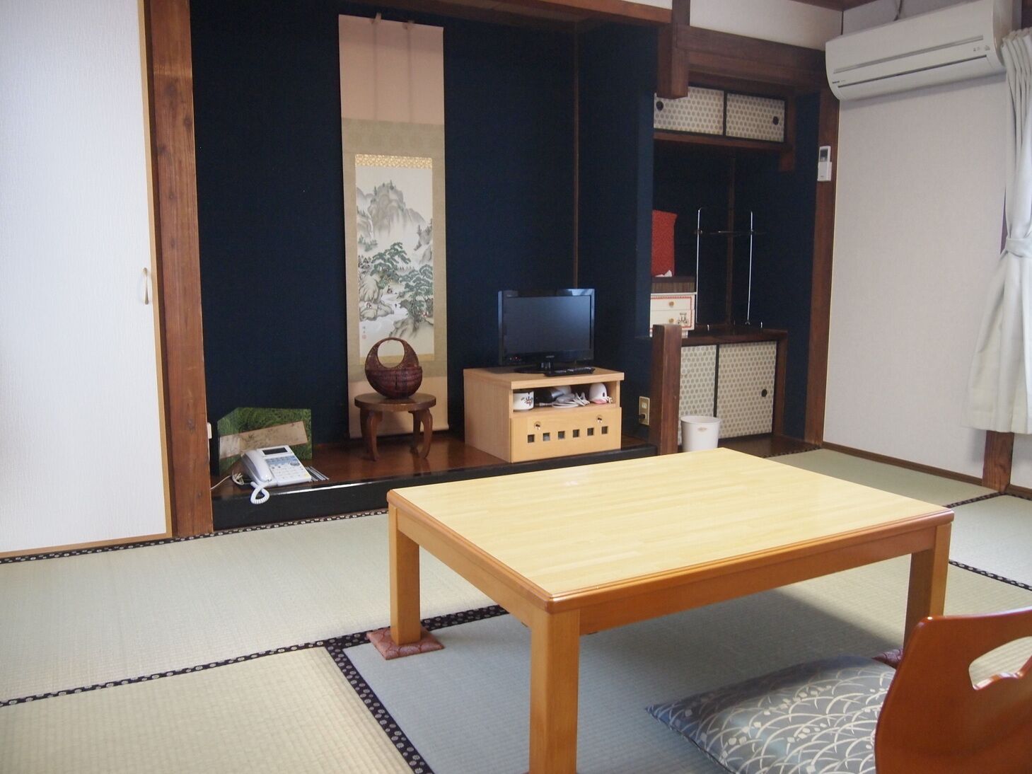 A traditional Japanese room with tatami flooring, a low table, a television, and a cabinet with storage.
