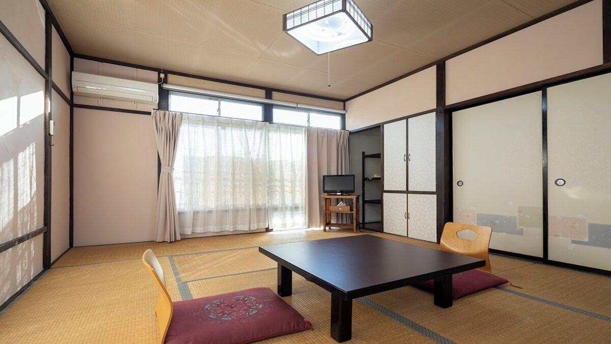 A traditional Japanese room with tatami flooring, a low table, a television, and sliding doors.