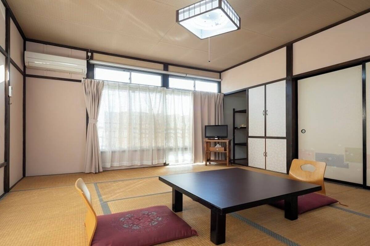 Ein traditioneller japanischer Raum mit Tatami-Böden, einem niedrigen Tisch, einem Fernseher und Schiebetüren.