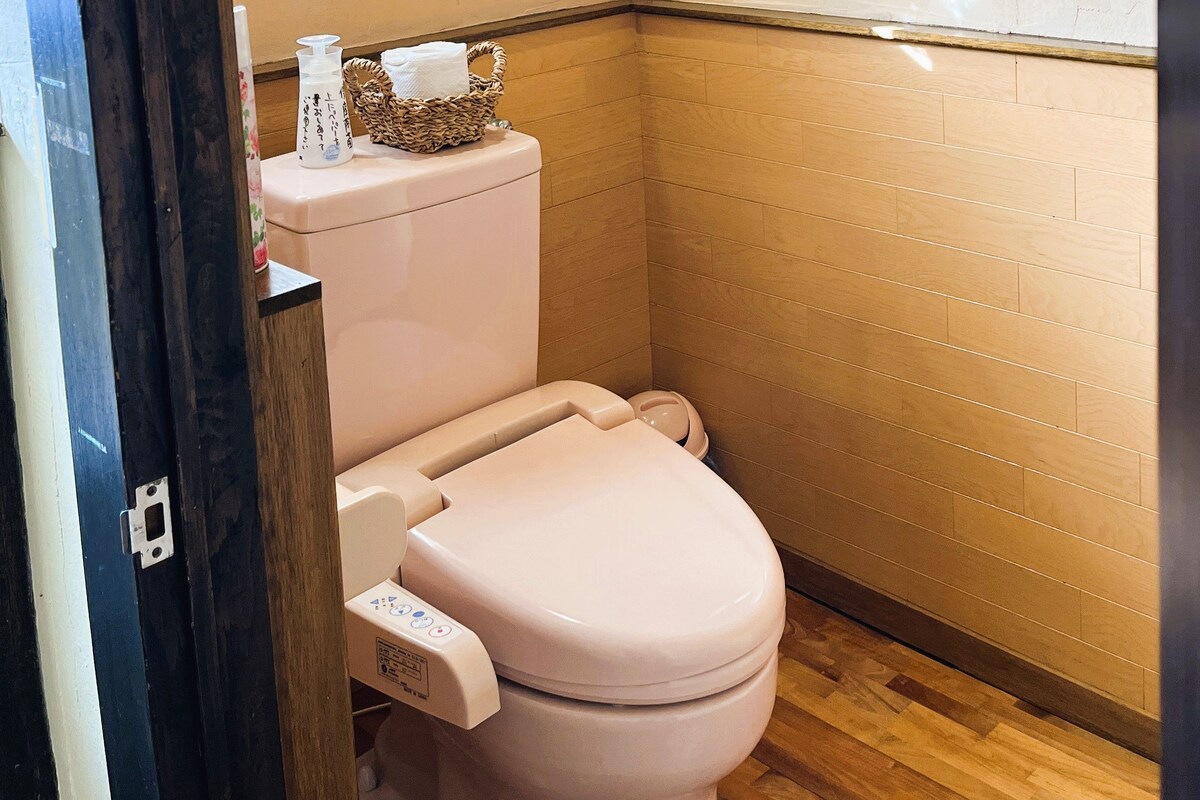 A small, modern bathroom with a toilet, a hand sanitizer dispenser, and a tissue holder on the wall.