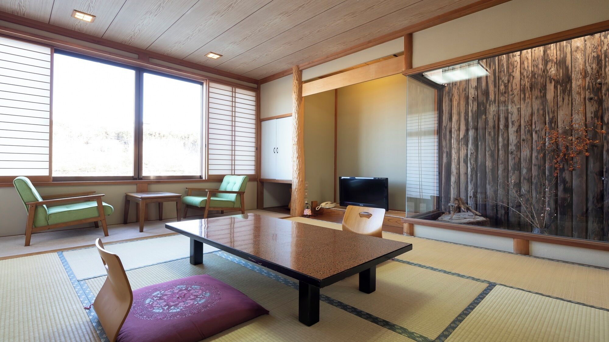 A traditional Japanese room with tatami flooring, a low table, chairs, a television, and a sliding door with a wooden backdrop.