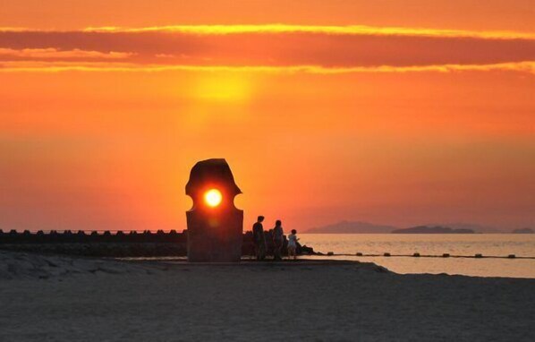 A sunset over a beach with a large stone structure, a pier, and a calm sea.