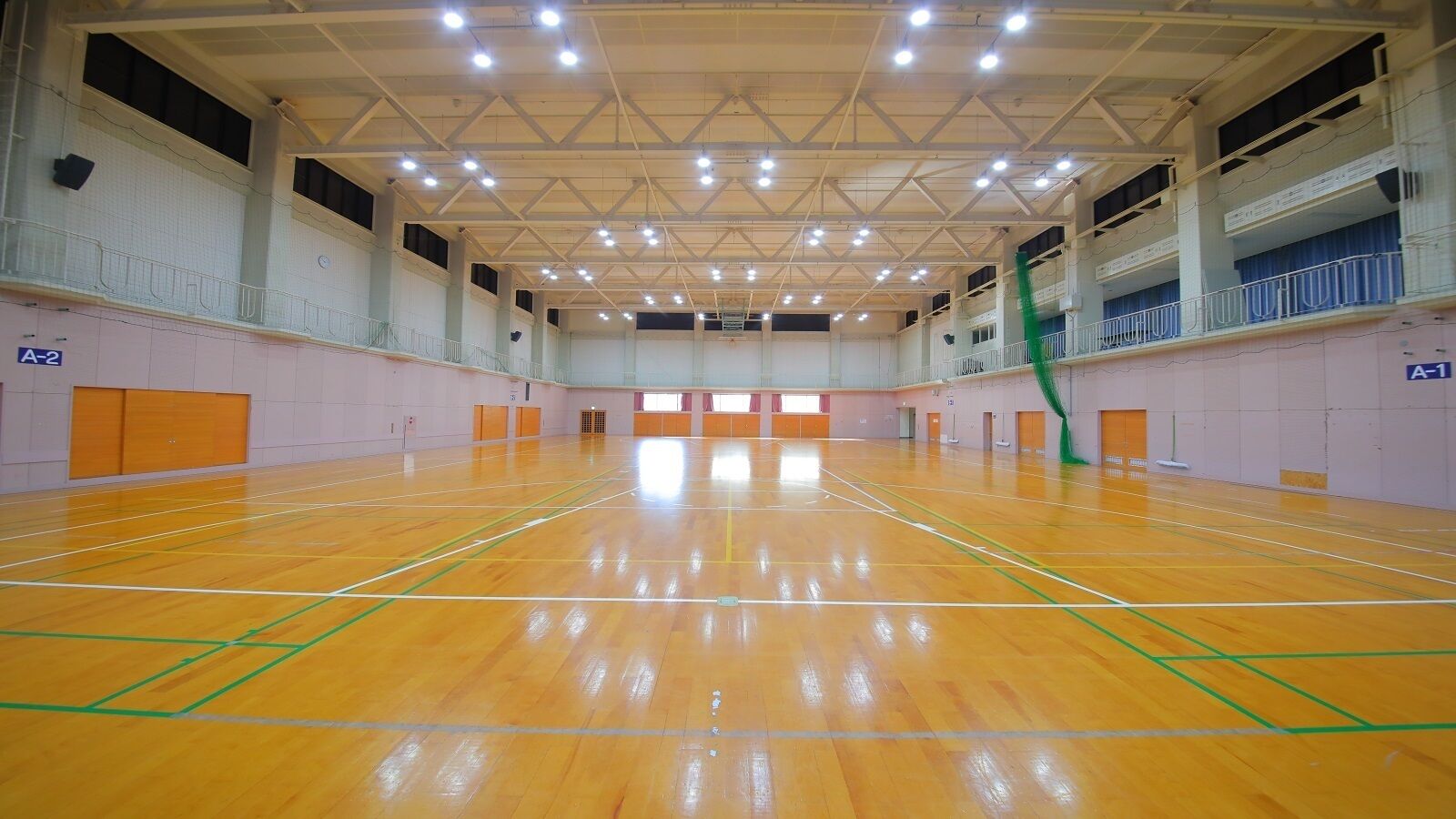 Un gimnasio interior con suelo de madera, varias canchas de baloncesto y un techo alto con iluminación.