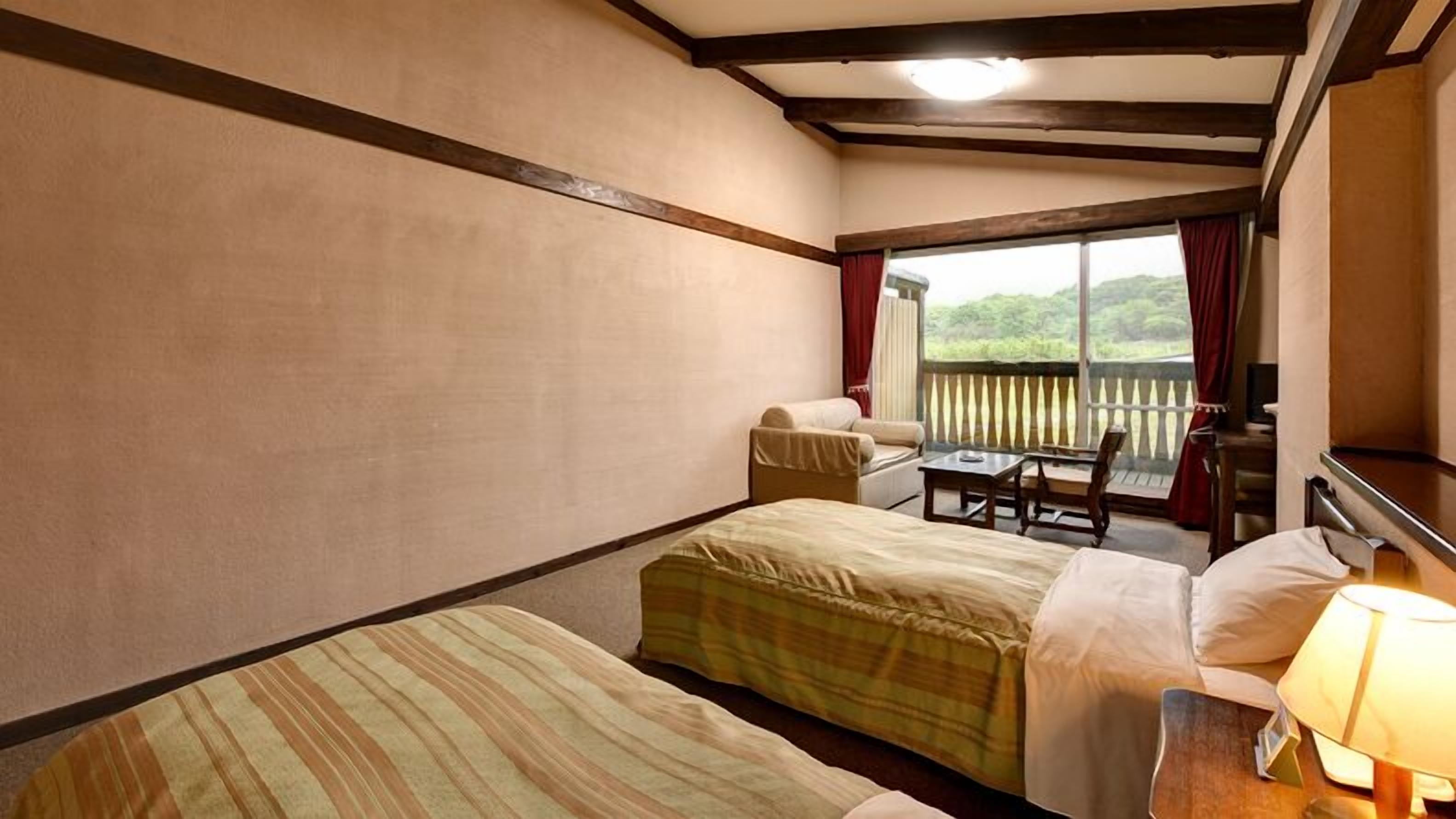 A hotel room with two beds, a small table, a chair, and a view of the outdoors.