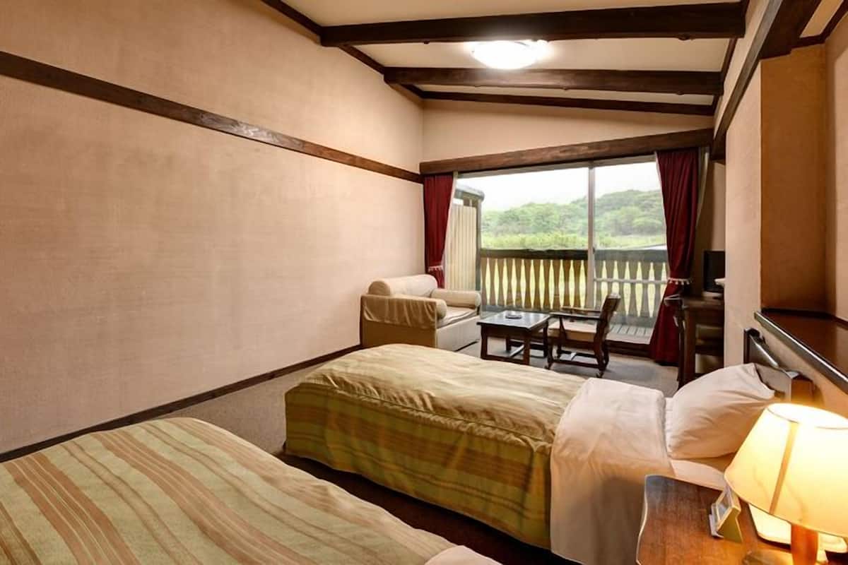 Ein Hotelzimmer mit zwei Betten, einem kleinen Tisch, einem Sessel und Blick ins Freie.
