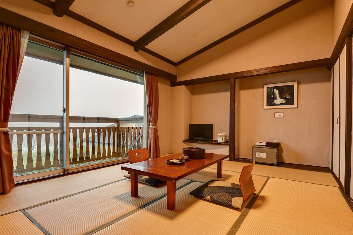 Ein traditioneller japanischer Raum mit Tatami-Boden, einer Schiebetür, einem Fernseher und einem kleinen Schrank.